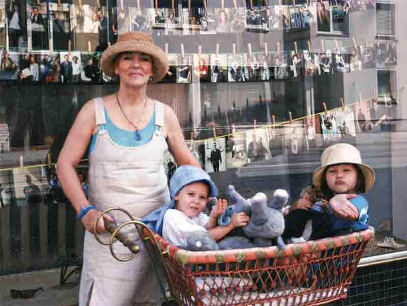 Eine stilvolle Frau schiebt elegant einen Korb mit zwei niedlichen Kindern vor dem Schaufenster des Urlaubsreif-Reisebüros in München.